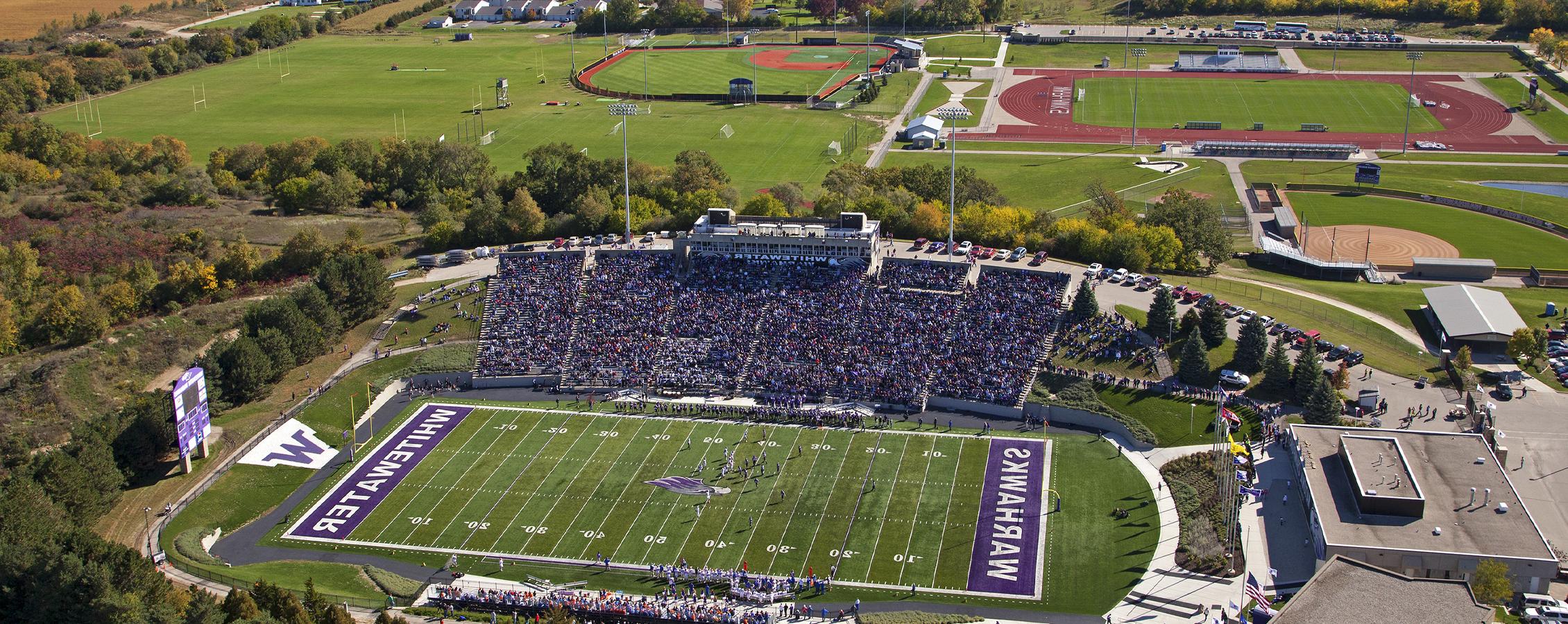 An aerial view of the football stadium, baseball diamond and track area surrounded by large trees.